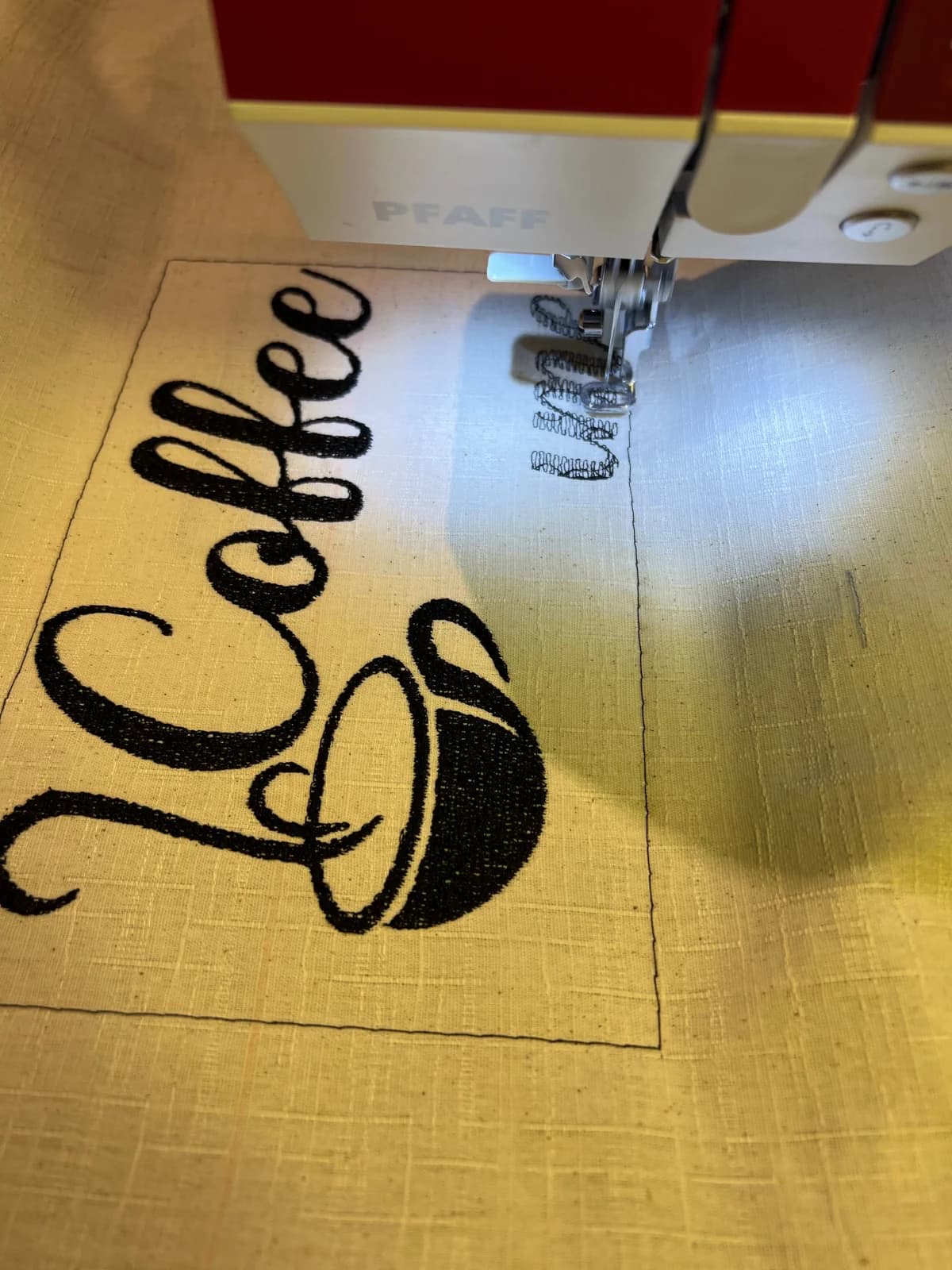 En broderimaskin syr et kaffemotiv på stoff